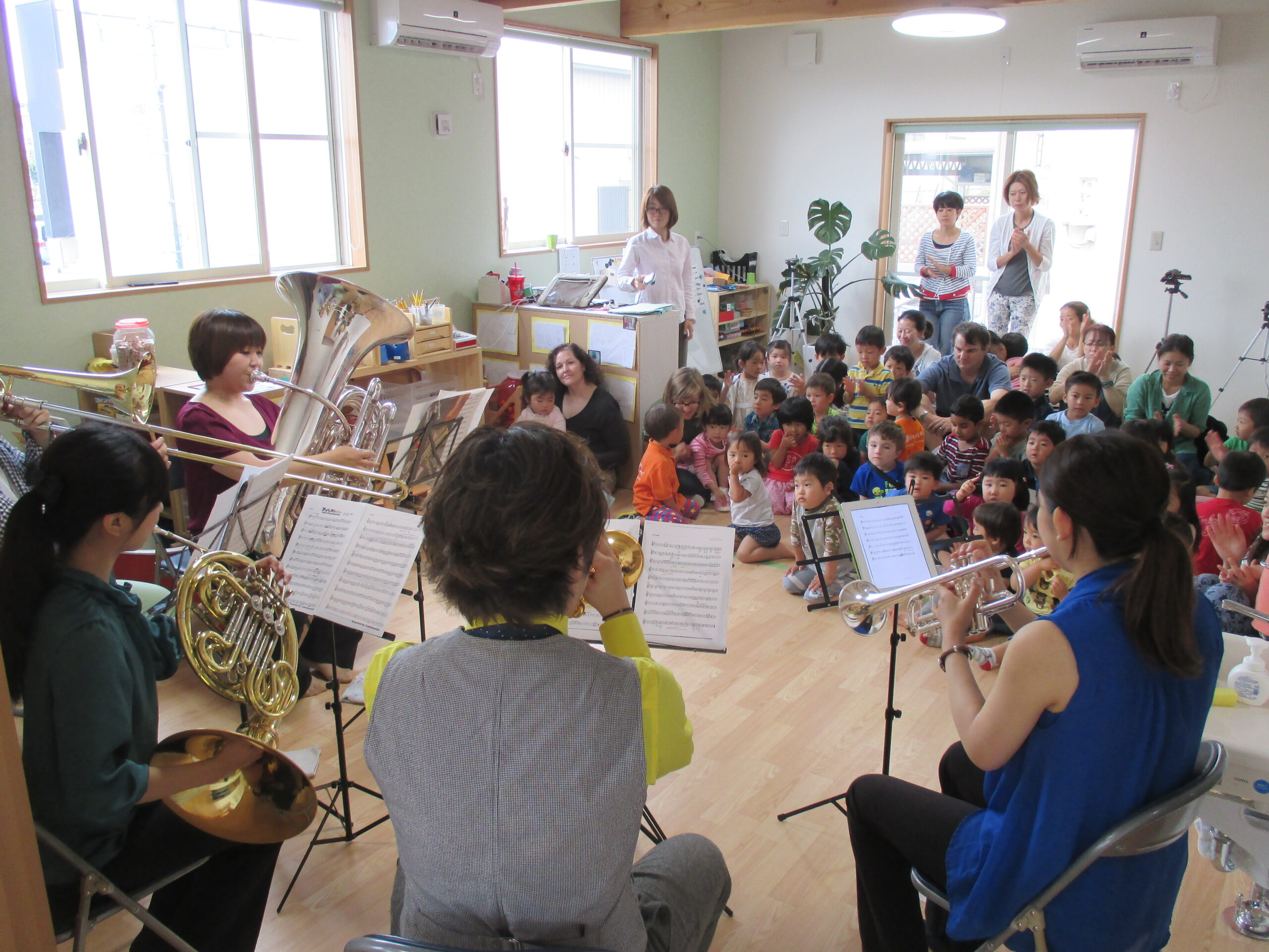 名古屋インターナショナルプリスクールの園児たちが金管バンド演奏を鑑賞 名古屋のインターナショナルプリスクールで、園児たちが音楽特別クラスの一環として金管バンドの生演奏を楽しんでいる様子。