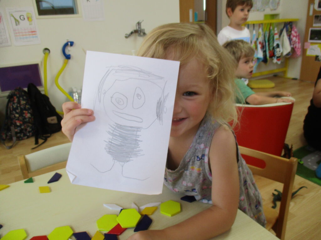 自画像を見せる笑顔の子ども|ディスカバリー・インターナショナルスクール 名古屋のディスカバリーインターナショナルスクールで、自分の似顔絵を描いて嬉しそうに見せる子ども。レッジョ・エミリアに基づいた国際幼稚園のアート活動。